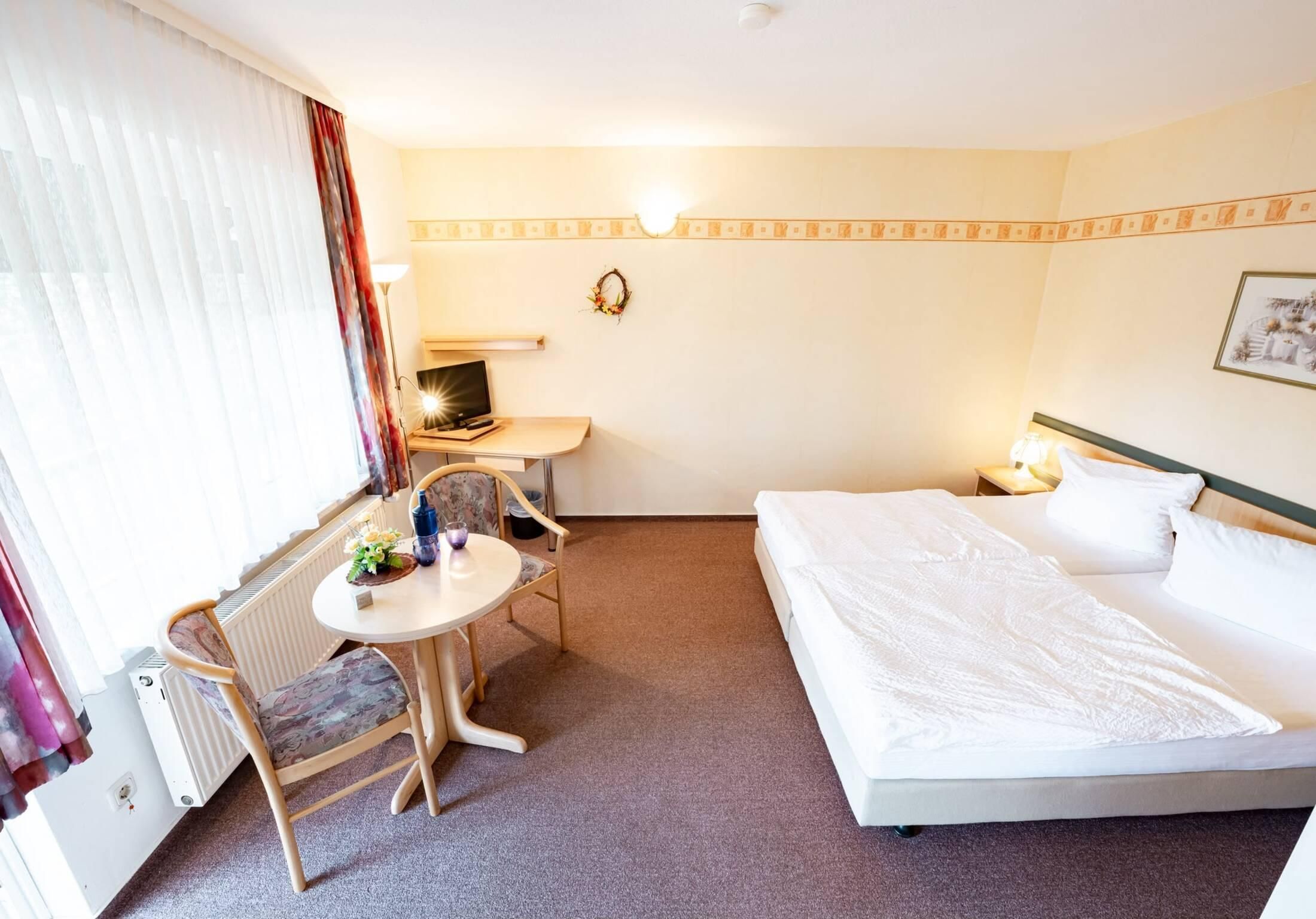 Una camera d'albergo con un letto, una scrivania, una sedia, un tavolo e un termosifone.