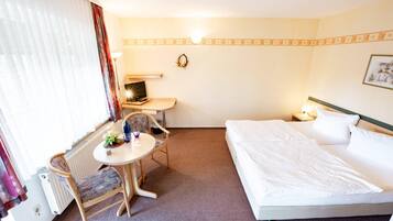 Una camera d'albergo con un letto, una scrivania, una sedia, un tavolo e un termosifone.
