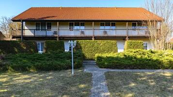 A two-story building with a red-tiled roof, a balcony on the upper floor, and a well-maintained garden with hedges and a gravel path leading to the entrance.
