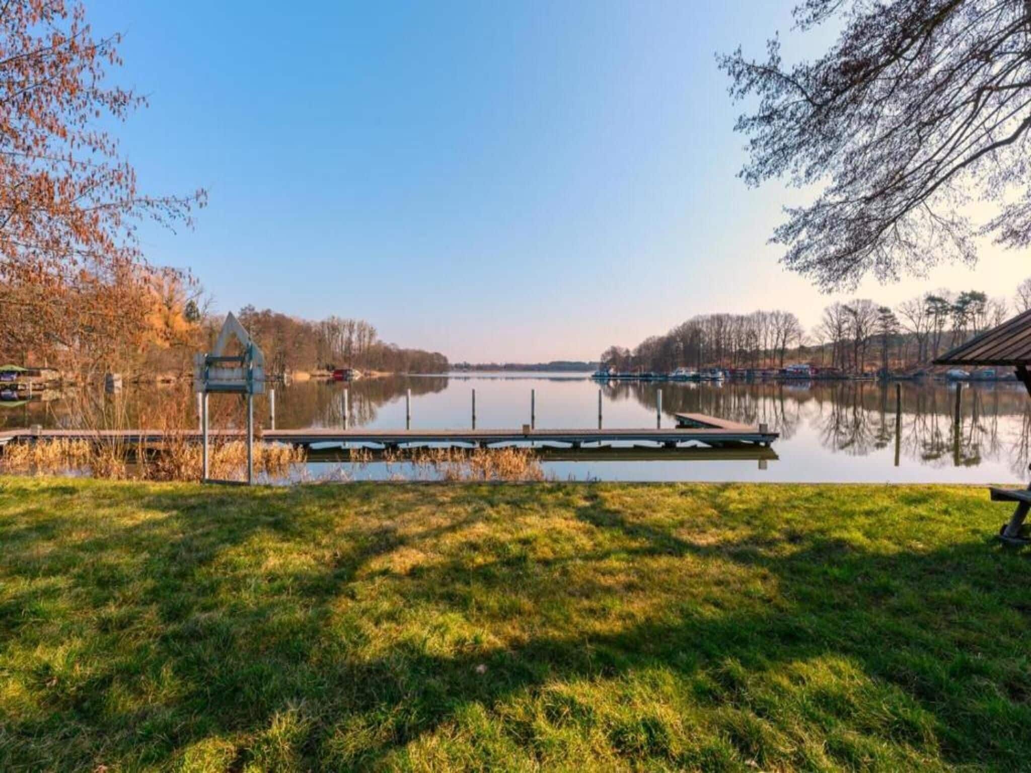 Un lago tranquilo con un muelle, zonas de césped y árboles al fondo.