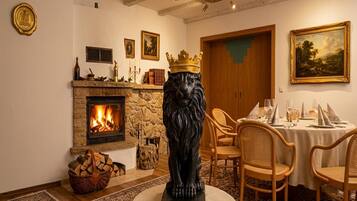 A room with a fireplace, a lion statue, a dining table set for two, and a painting on the wall.