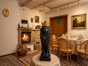 Una habitación con chimenea, una estatua de león, una mesa de comedor lista para dos personas y un cuadro en la pared.
