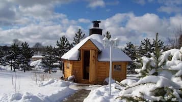 A wooden cabin with a snow-covered roof, a chimney, and a small porch.