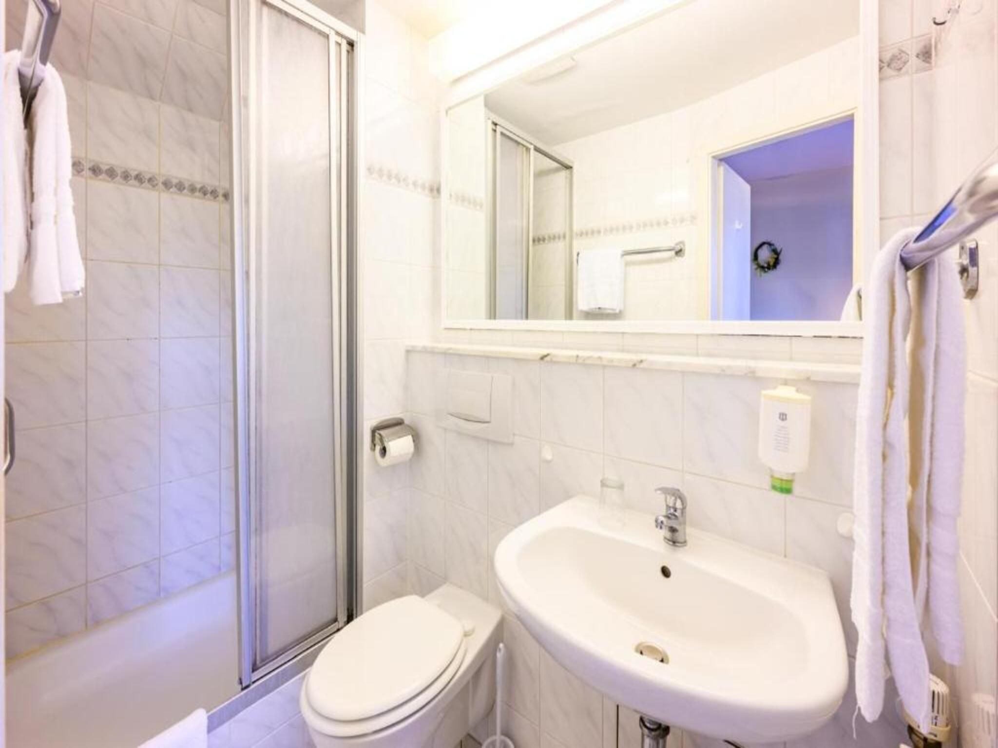 A bathroom with a shower, toilet, sink, and a mirror.