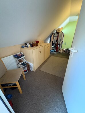 Una habitación pequeña con una silla, un armario y una escalera que lleva a otra habitación.
