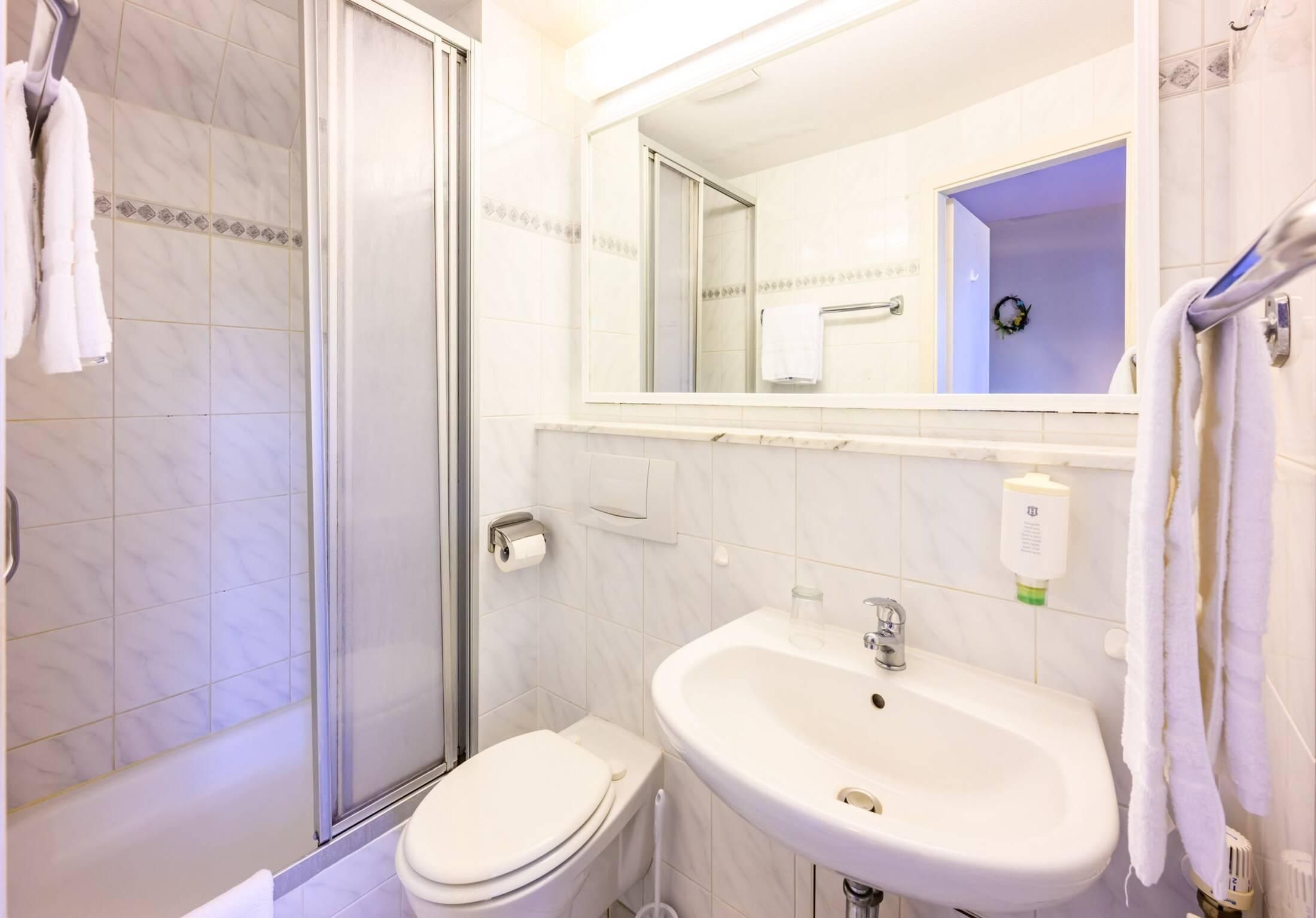 Et badeværelse med brusekabine i glas, toilet, vask og spejl.