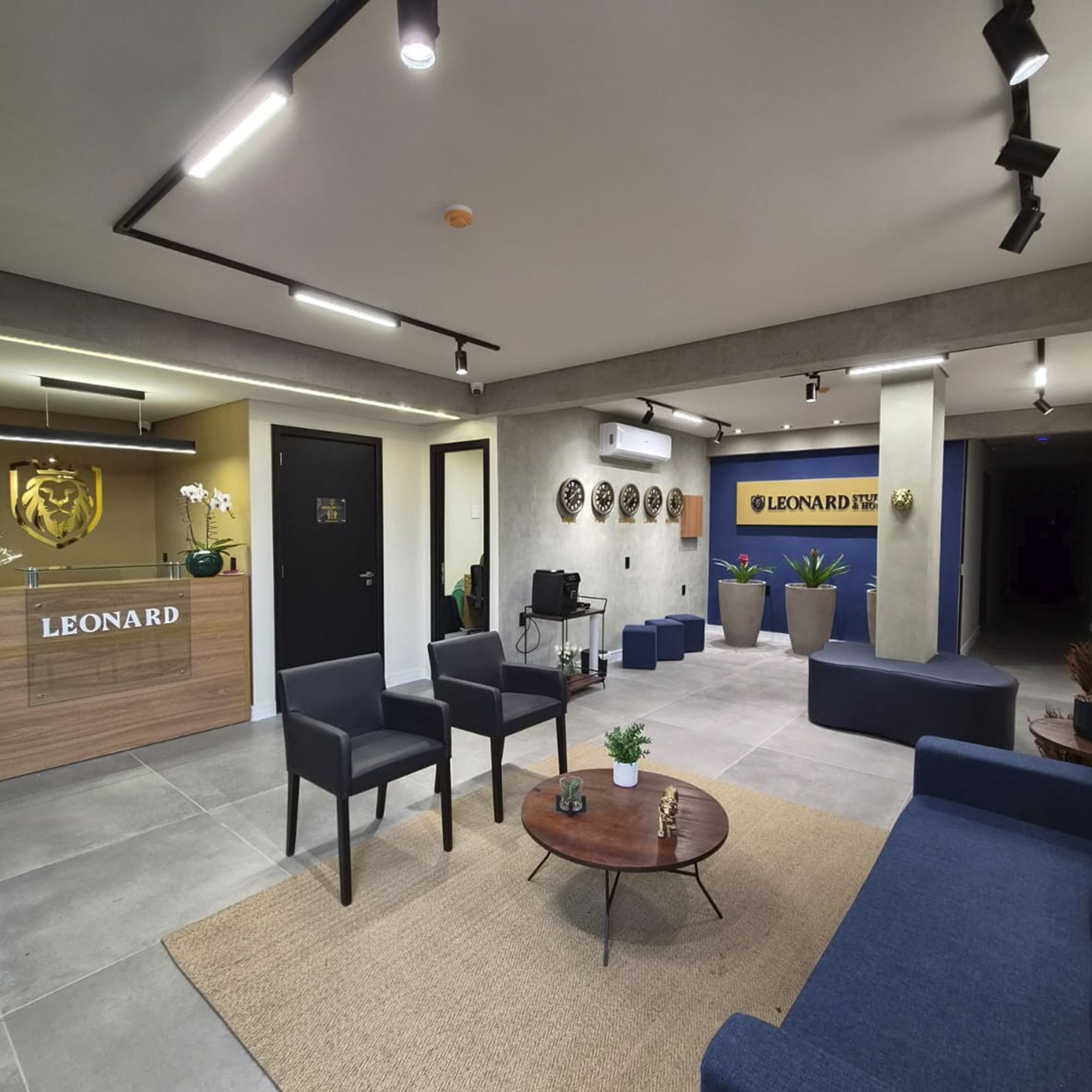 Un interior moderno con mostrador de recepción, zona de estar y una pared decorada con relojes.
