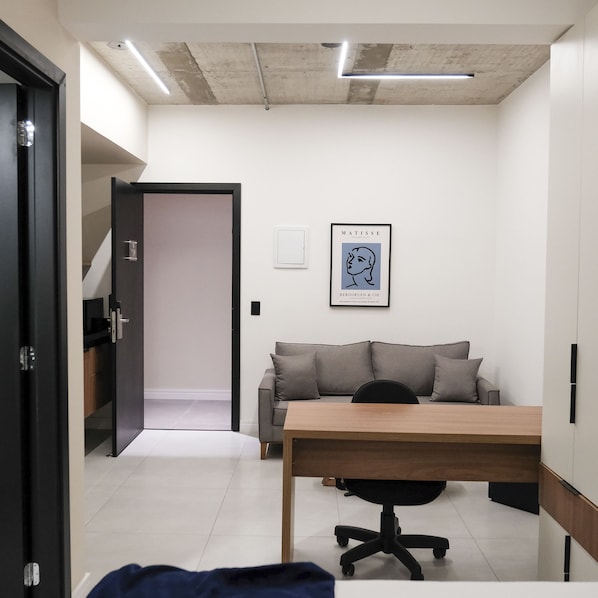 Un espacio de oficina moderno con un escritorio, una silla de oficina y un sofá gris.
