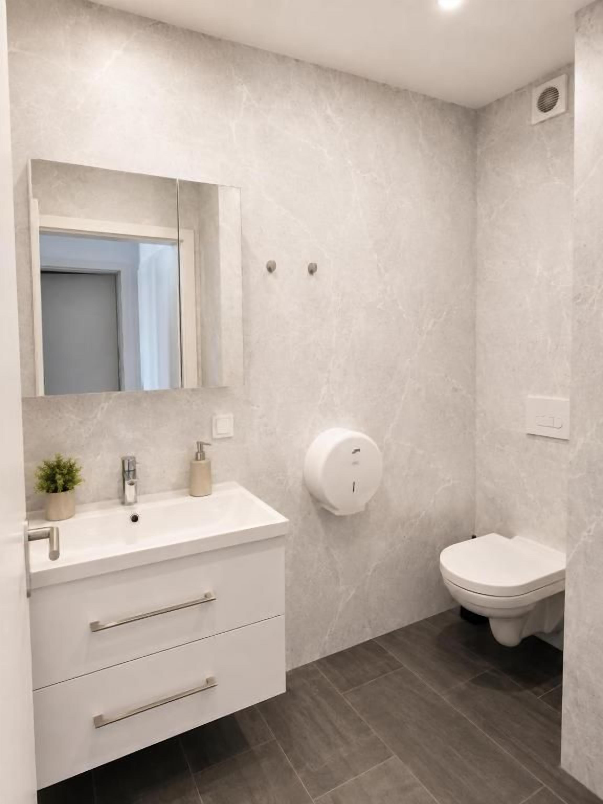 Ein Badezimmer mit einem weißen Waschtisch, einer Toilette und einem an der Wand befestigten Seifenspender.