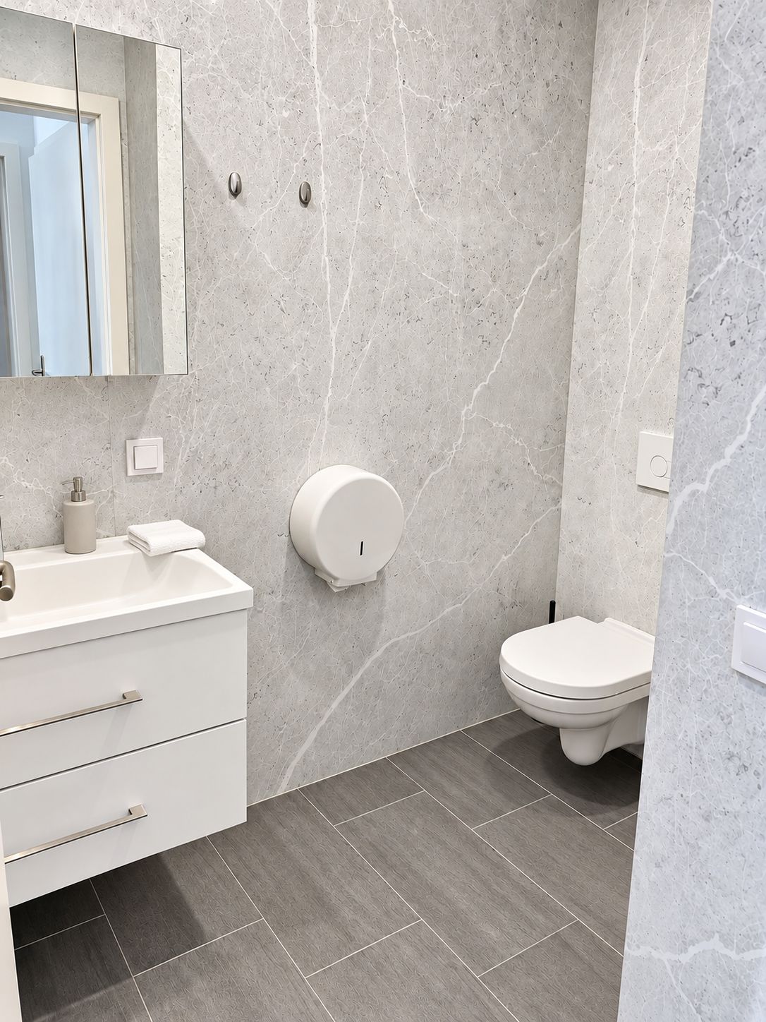 Ein Badezimmer mit weißem Waschtisch, Toilette und Wandseifenspender.