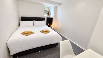 A hotel room with a bed, a bedside table with a lamp, a chair, and a small window.