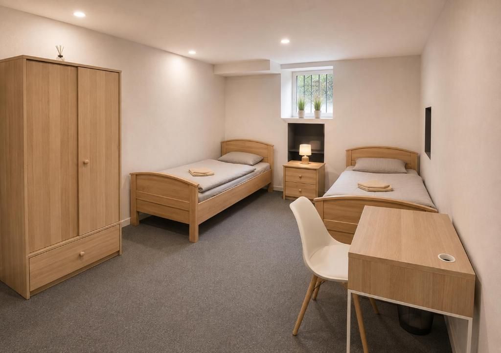 Ein Schlafzimmer mit zwei Einzelbetten, einem Holzschrank, einem Schreibtisch mit Stuhl und einem kleinen Fenster mit Pflanzen.