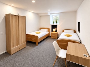 A compact bedroom with two single beds, a wooden wardrobe, a desk, and a chair.