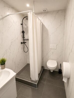 Un baño moderno con ducha, inodoro y lavamanos blanco.