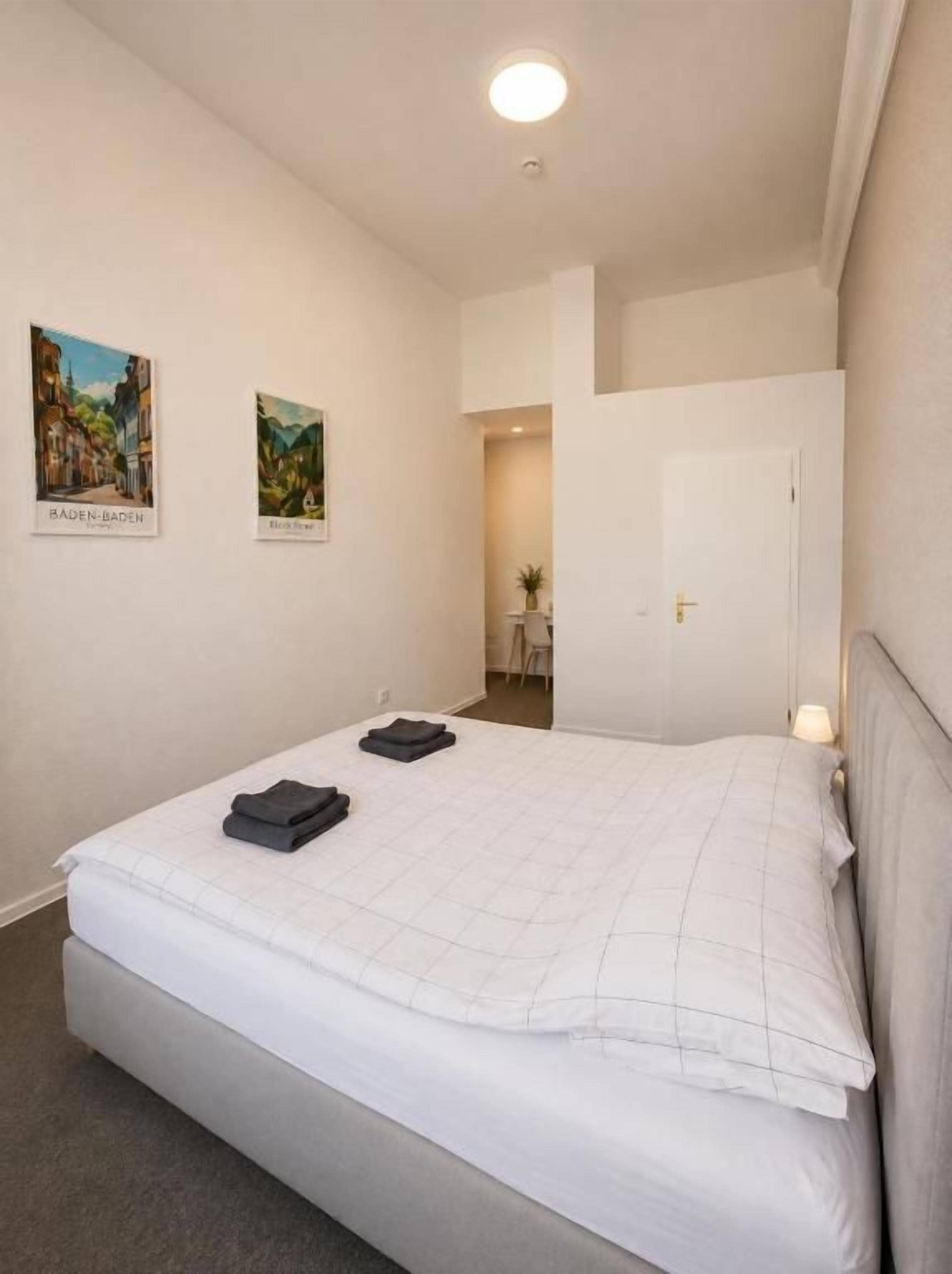 Ein Hotelzimmer mit einem Bett, einem Nachttisch, einer Lampe und zwei gerahmten Bildern an der Wand.