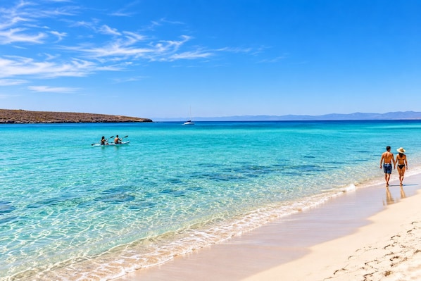 A beach with clear turquoise water, a sandy shore, and a distant sailboat.