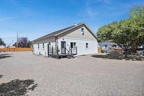 A single-story building with a gravel driveway, a covered outdoor area, and a tree to the right.