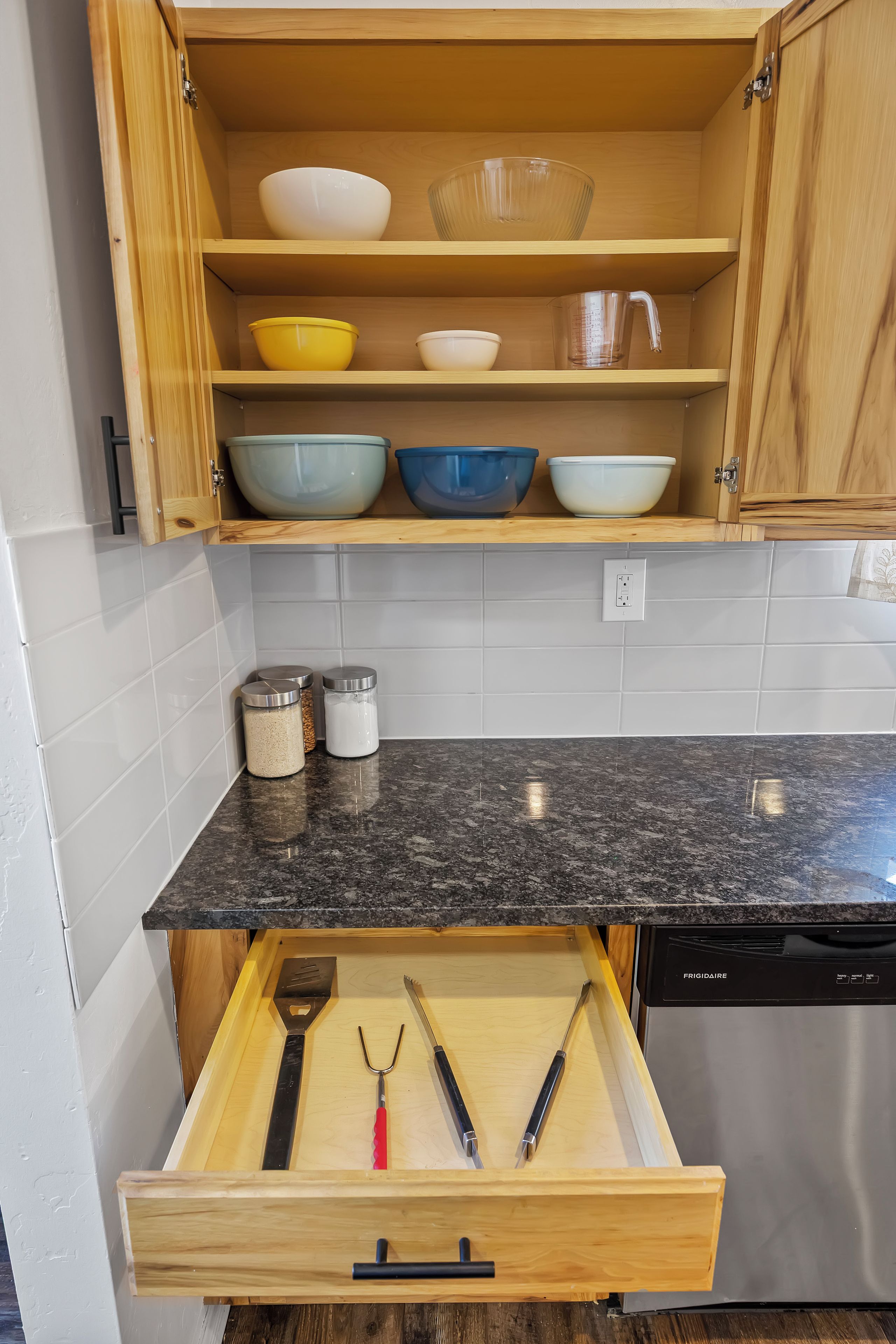 Eine Küche mit Holzausstattung, einer Arbeitsplatte aus Granit und einer Schublade mit Küchenutensilien.