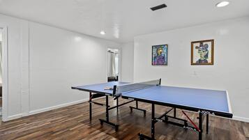 A room with a ping pong table, wooden flooring, white walls, and two paintings.