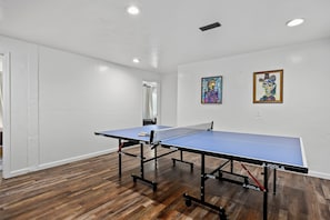A room with a ping pong table, wooden flooring, white walls, and two paintings.