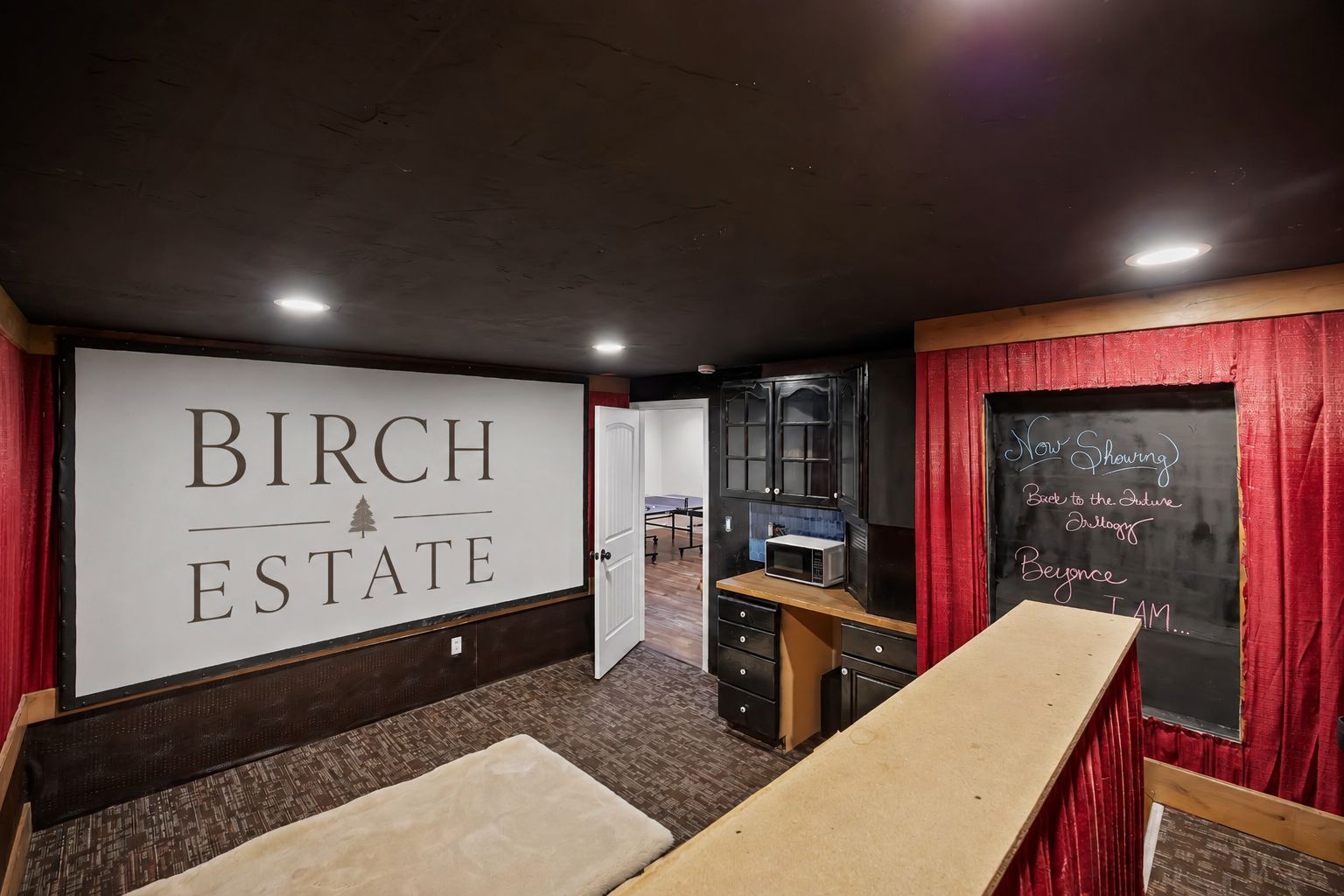 A room with a large screen displaying 'BIRCH ESTATE' and a chalkboard with 'Now Showing' and 'Back to the Future' text.