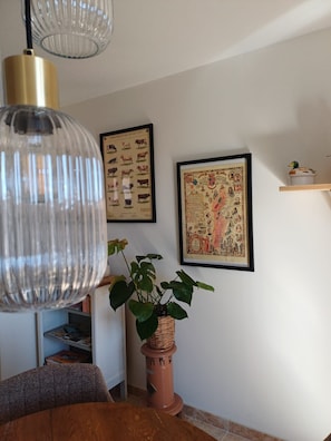 A room with a dining table, a potted plant, a hanging light fixture, and two framed pictures on the wall. - The Burgundian Interlude (Rigny-sur-Arroux)