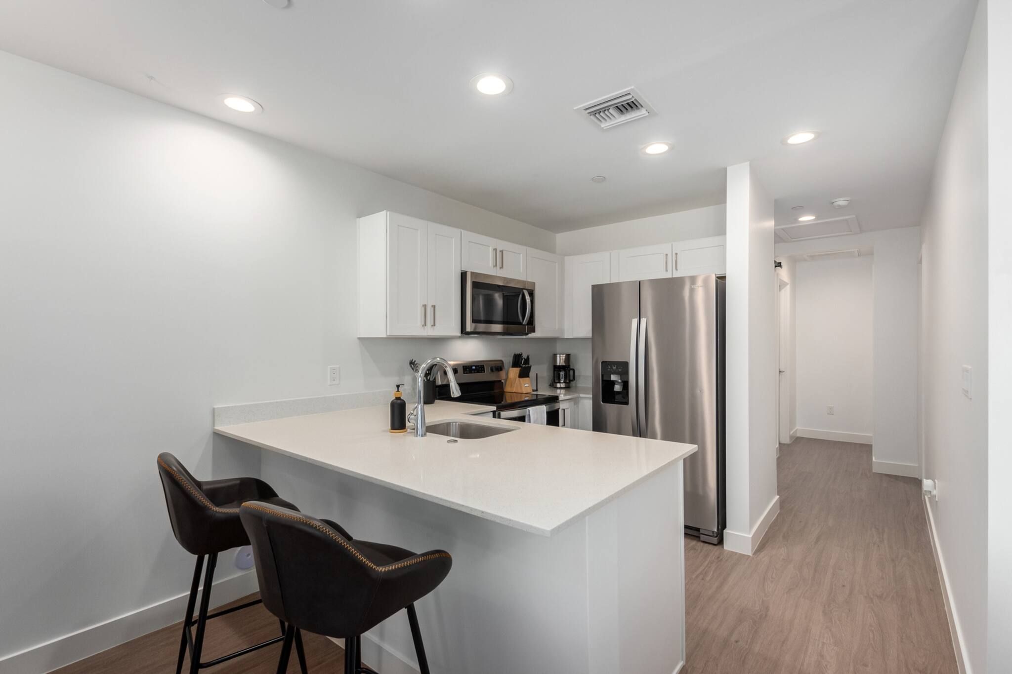 A modern kitchen with white cabinetry, stainless steel appliances, and a central island with two bar stools.