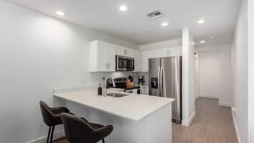 A modern kitchen with white cabinetry, stainless steel appliances, and a central island with two bar stools.