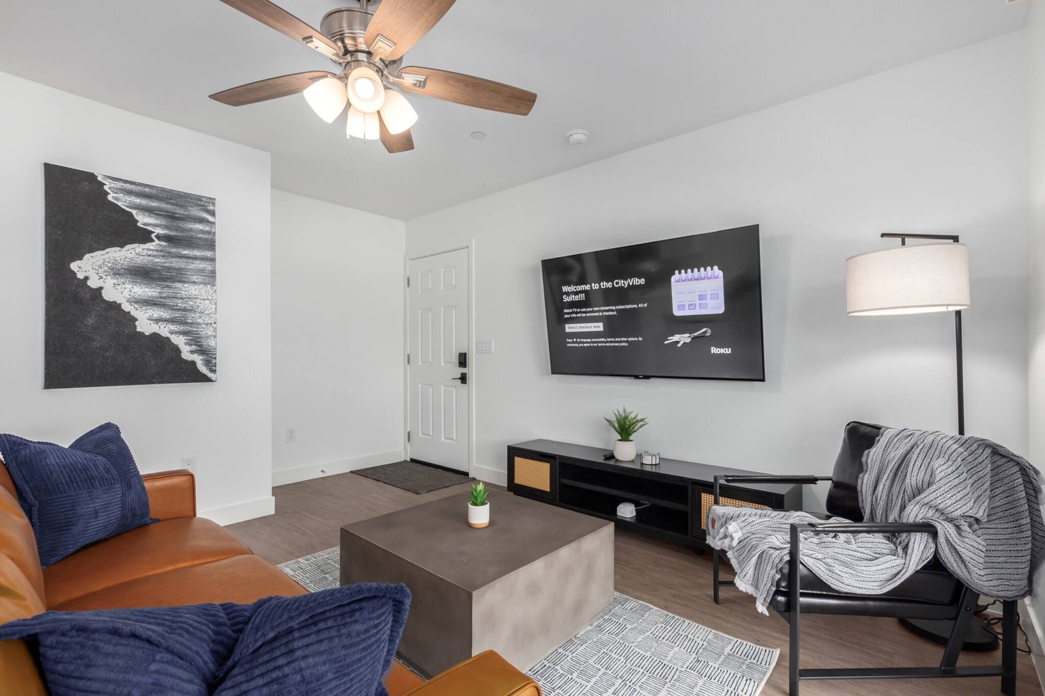 A modern living room with a ceiling fan, a flat-screen TV mounted on the wall, a sofa, a coffee table, and a chair.