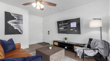 A modern living room with a ceiling fan, a flat-screen TV mounted on the wall, a sofa, a coffee table, and a chair.