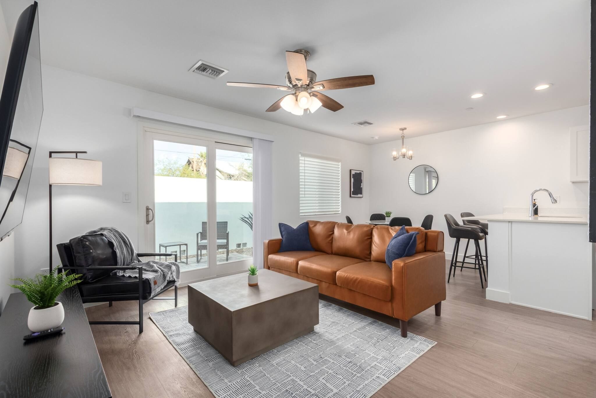 A modern living room with a leather sofa, a coffee table, and a dining area with a kitchen in the background.