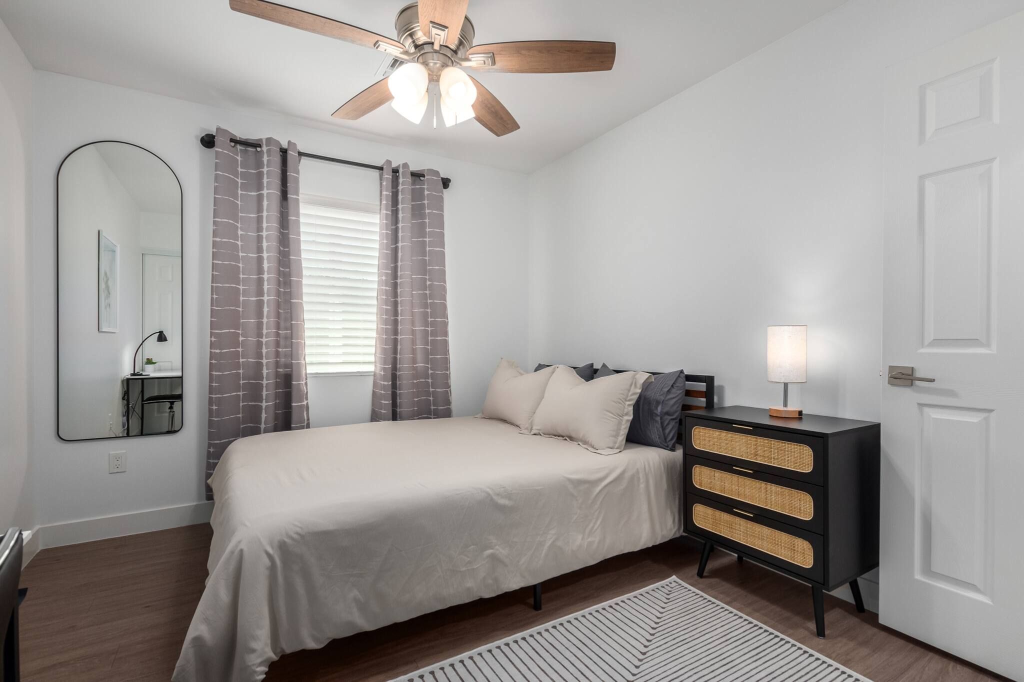 Une chambre à coucher avec un lit, une commode, un miroir et un ventilateur de plafond.