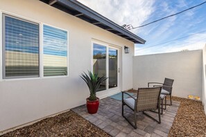 Eine Terrasse mit Glastür, einem roten Blumentopf und zwei Korbstühlen.