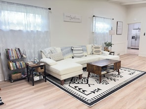 A living room with a sectional sofa, a coffee table, a bookshelf, and a patterned rug.
