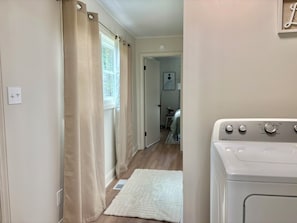 A laundry room with a washing machine, a door leading to another room, and a window with curtains.