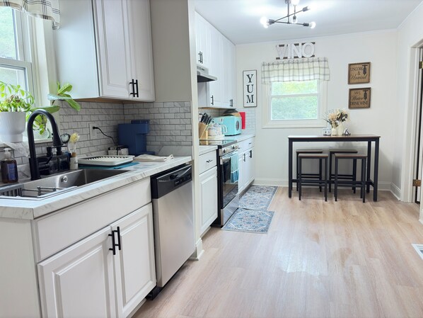 A kitchen with white cabinetry, a dishwasher, a sink, and a dining area with a table and stools.