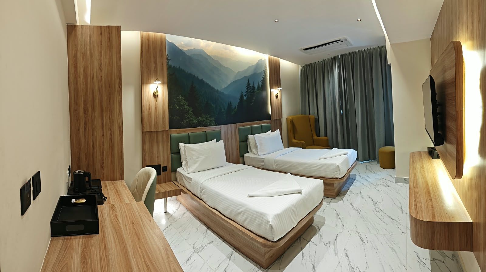 A hotel room with two beds, a desk, a chair, a TV, and a large painting of a mountain landscape.