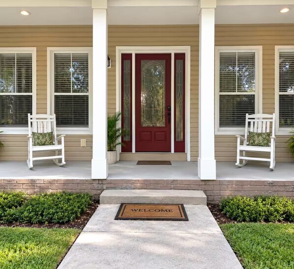 A house with a red door, two white rocking chairs on the porch, and a welcome mat.