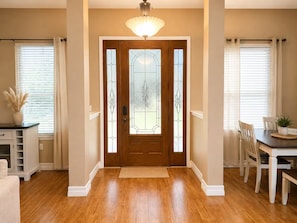 A hallway with a wooden door, a dining area with a table and chairs, and a ceiling light fixture.