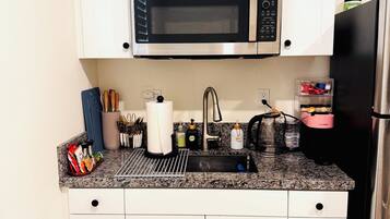 A compact kitchen with white cabinets, a stainless steel microwave, a black refrigerator, and a granite countertop.