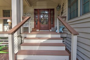 A wooden staircase leading to a front door with a glass panel, a welcome mat, and a wall-mounted bird sculpture. - Renovated Sea Pines Retreat with Private Pool (Hilton Head Island)