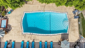 An aerial view of a rectangular swimming pool with a surrounding deck, lounge chairs, and a small shaded area. - Desert Days & Poolside Ways | 1BR Suite (Palm Springs)