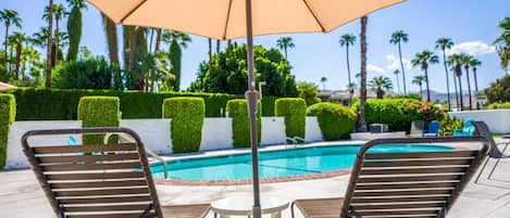 A poolside area with two lounge chairs, a table, and a large umbrella.