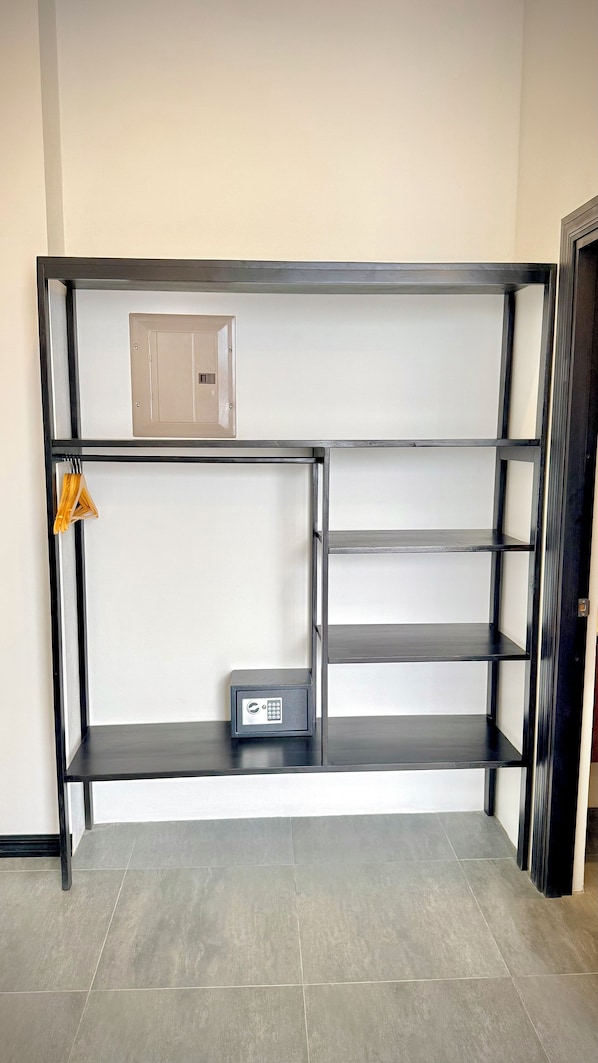 A metal-framed, open shelving unit with a small safe and a hanging garment rack. - Hotel Plaza Iguana (Quepos)
