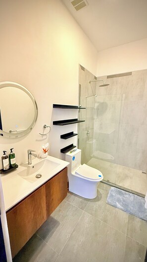 Un baño moderno con un espejo redondo, un lavabo, un inodoro y una ducha con mampara de vidrio.
