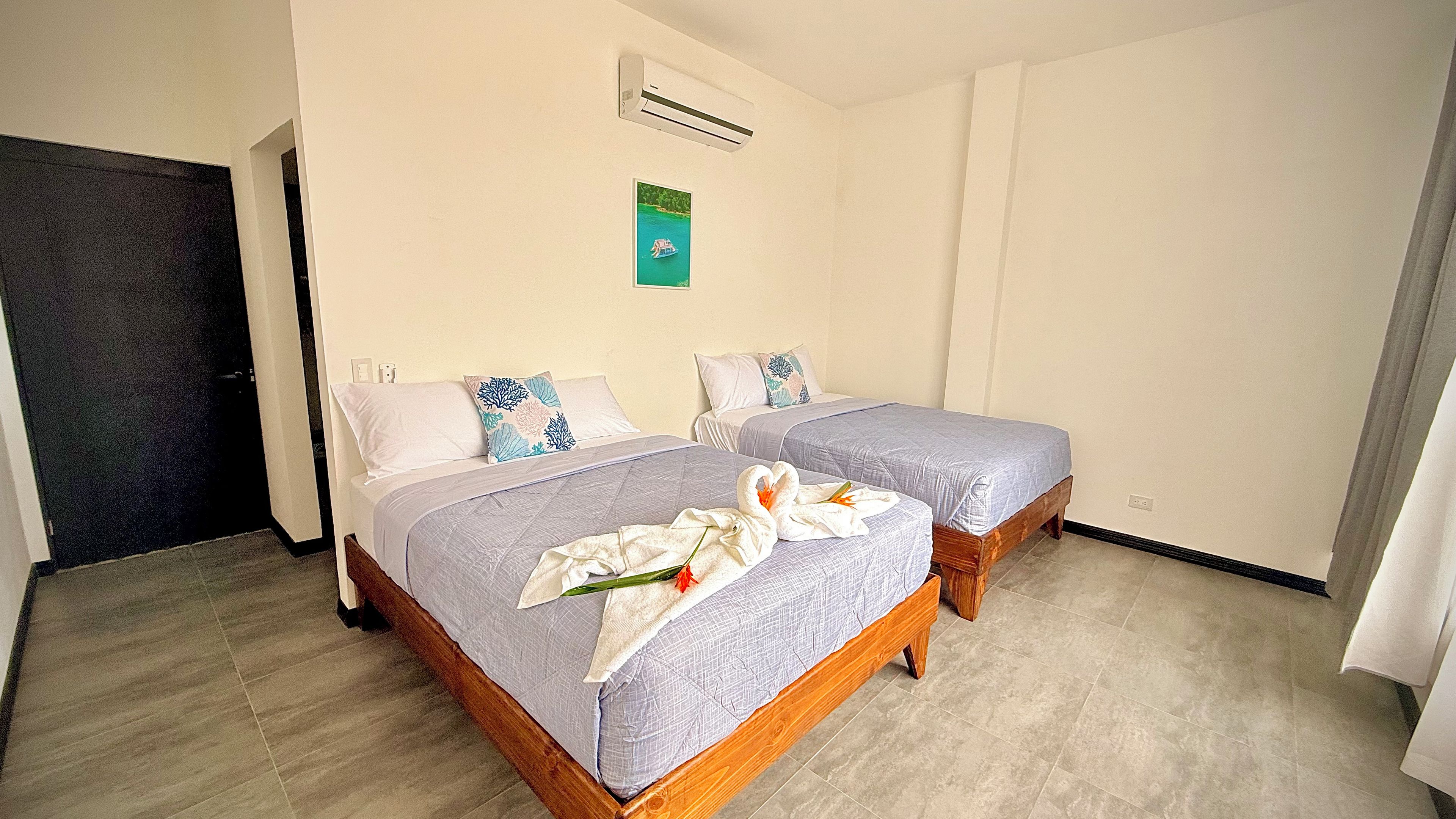 Quarto de hotel com duas camas, piso de madeira, ar-condicionado fixado na parede e um quadro emoldurado.