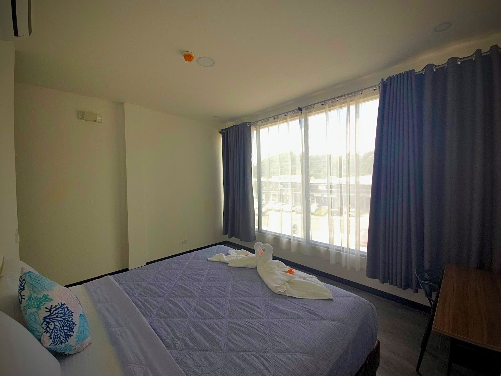 Quarto de hotel com uma cama grande, janela com cortinas, escrivaninha e uma cadeira.