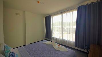 Quarto de hotel com uma cama grande, janela com cortinas, escrivaninha e uma cadeira.