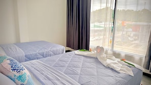 A hotel room with two beds, a window with curtains, and a view of the street outside. - Hotel Plaza Iguana (Quepos)