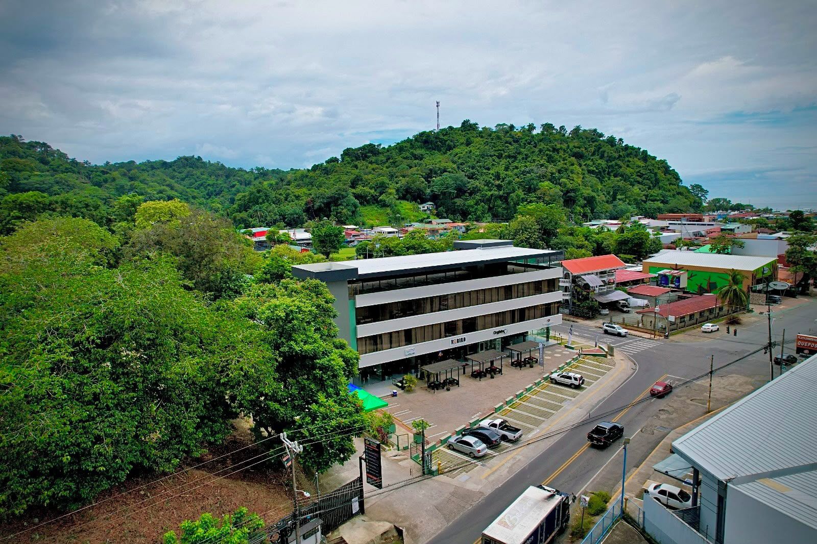 Edifício moderno de vários andares, rodeado por vegetação exuberante e uma paisagem montanhosa.